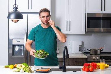 Modern mutfakta tek başına sağlıklı yemekler hazırlayan, salata pişiren bir adam. Yakışıklı adam evdeki mutfakta taze vegan salatası hazırlıyor. Sağlıklı yemek sağlıklı hayattır.