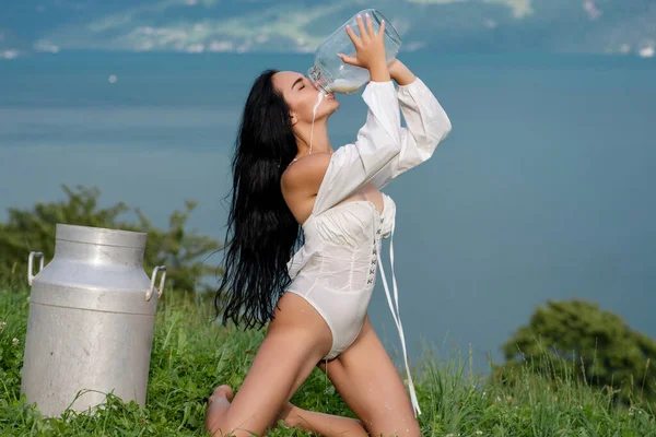 Sexy woman in lingerie drink milk from can and bottle against countryside. Sexy woman drinking milk in Alps. Sensual woman eat milk near Swiss Alps. Beautiful woman enjoys milk on alpine village