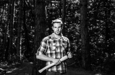 Sakallı yakışıklı bir genç adam ağaç taşıyor. Oduncu gibi poz veren şık bir genç adam. Oduncu işçi balta ile ormanda yürüyor.