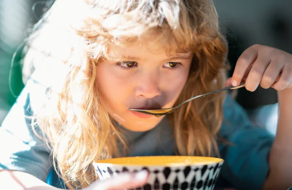 Cute child eats food itself with spoon. Little kid are eating soup, closeup kids face