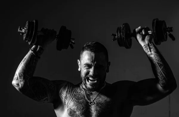 若い筋肉ボディービルダーの男は暗い背景の上にダンベルで演習を行う 激しいトレーニング — ストック写真