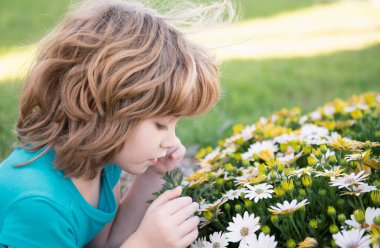Bahar çocuğu suratı. Bahar çiçekli küçük sarışın bir çocuğun portresi. Arka bahçedeki komik çocuklar. Çocuklar çiçek arkaplanda yüzlerini kapatırlar. Çocuklar bahar çiçeklerinde oynar.