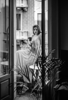 Balkonda elinde kahve cevheri çayı tutan genç bir kadın. Güzel bir kadın sabah villanın balkonunda temiz hava soluyor. Güzel kız tazeliğin tadını çıkarıyor.