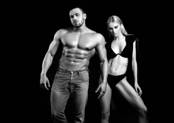 Fitness couple over black background. Fit fashion couple posing. Beautiful sexy couple in love dressed in blue jeans. Passionate couple in studio