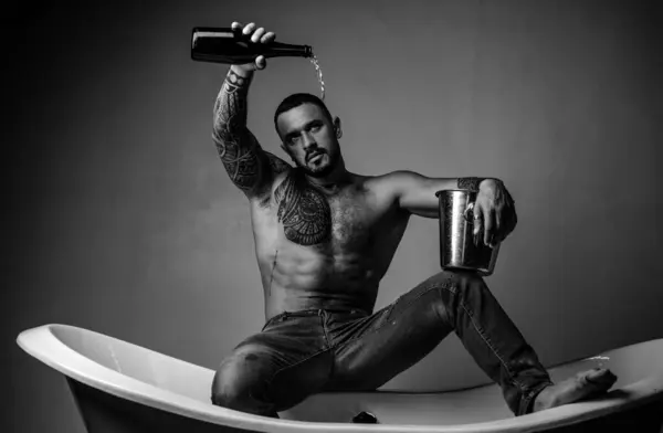 Night party. Celebrate purchase real estate. Celebrate luxury life. Celebrate achievement. Champagne celebration in luxury bathtub. Handsome attractive man tattooed body drinking expensive champagne.