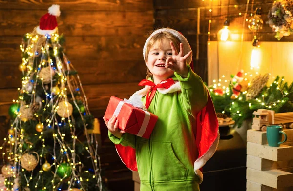 Noel Ağacının Yanındaki Mutlu Çocuk Elinde Noel Hediyesiyle Kameraya Bakıyor — Stok fotoğraf