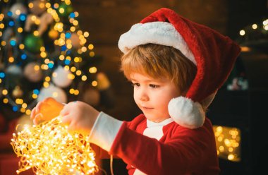 Noel arifesinde Noel ağacı ve şöminesinde çelenk ışıkları olan bir çocuk. Bu bir mucize. Noel 'i evde kutlayan çocuklu bir aile. Sevimli çocuk neşeli ruh hali Noel ağacının yanında oynuyor.