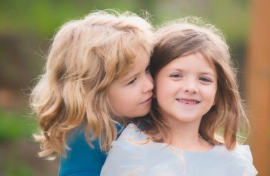 Çocuk ve kız bahar bahçesinde birbirlerine sevgiyle sarılıyorlar. Parkta sarılan iki küçük çocuk. Çocuklar dışarıda beraber oynuyorlar. Küçük kız parkta küçük çocuğu öpüyor.