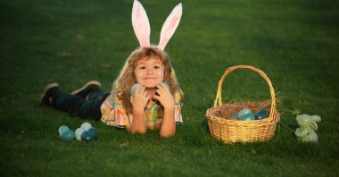 Child boy hunting easter eggs in spring lawn laying on grass. Bunny kids with rabbit bunny ears