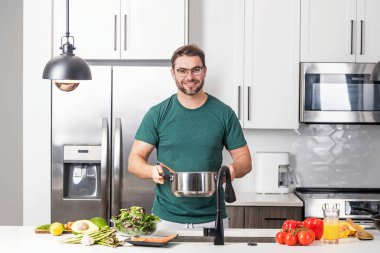 Adam mutfakta yemek pişiriyor. Şef aşçı tencereli bir yemek hazırlıyor. Menü tarifi sağlıklı yemek. Evde yemek pişiren adam mutfakta yemek hazırlıyor. Olgun bir adam mutfakta yemek hazırlıyor.