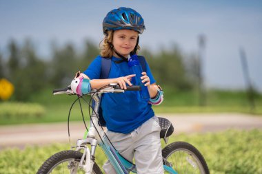 Parkta bisiklete binen sportif bir çocuk. Bisiklet süren kasklı çocuk. Çocuk bisiklet sürmeyi öğreniyor. Bisikletli çocuklar. Kasklı mutlu çocuk dışarıda bisiklet sürüyor. Çocuklarla spor eğlencesi.