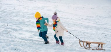 Mutlu çocuklar kışın karlı ormanlarda kızakla gezip eğleniyorlar. Kış Noel tatili ve aktif kış tatili, çocuk aktiviteleri. Kar arkaplanı, pankart kopyalama alanı