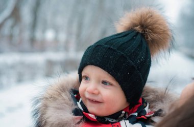 Funny laughing baby in winter outside. Cute toddler kid in a warm snowsuit and hat discovered winter forest. Snow, red cheeks, smile on face