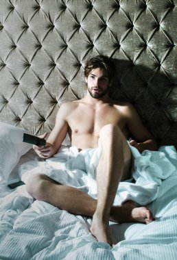 Yataktaki adam. Çıplak seksi erkek model, yatak odasında tek başına yatıyor.