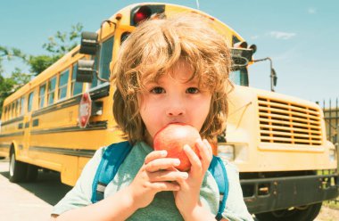 Okula dönelim. Okul otobüsünün önündeki çocuk elma yiyor.