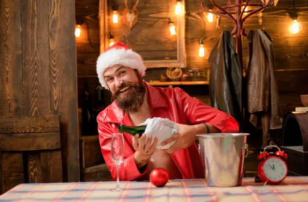 Happy smiling bearded Santa Claus pushes champagne down in glass. Merry Christmas and Happy Holidays. Amazing Christmas decorated background and lights. Christmas time concept