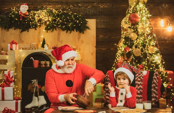 Father and son make a Christmas cookie on wooden house background. Santa helper. Little santa claus make cookie for Santa. Cute little son with father celebrating Christmas