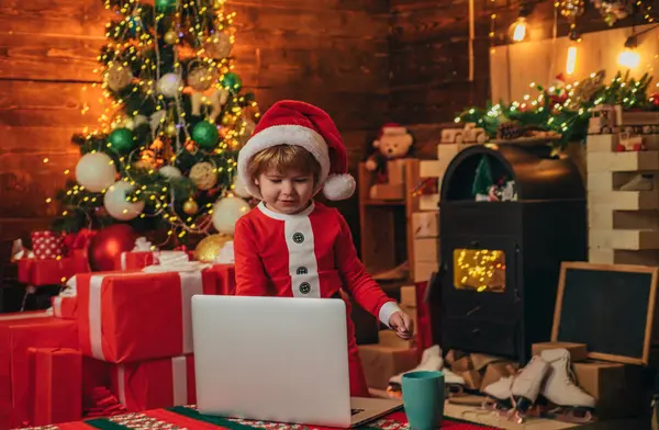 Little genius. Santa little helper. Little boy santa hat and costume having fun. Boy child with laptop near christmas tree. Buy christmas gifts online. Christmas shopping concept. Gifts service.