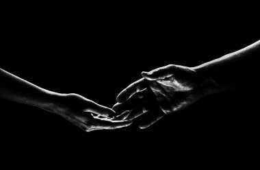 Two hands reaching toward. Helping hand outstretched for salvation on isolated black background. Close up of man and woman hand touch with fingers. Man and woman holding hands
