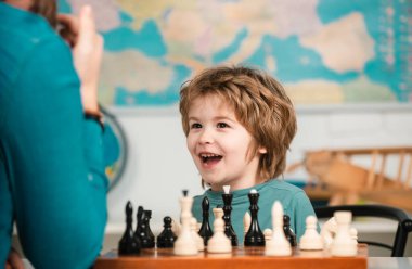Çocuk satranç okulu. Neşeli gülümseyen küçük çocuk masada oturuyor ve akşam keyfi ile satranç oynuyor.