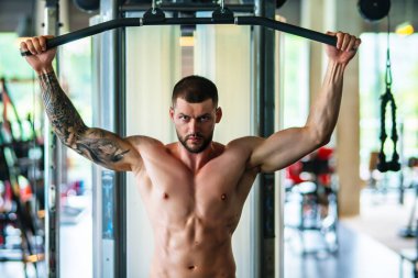 Spor salonunda poz veren kaslı iri kıyım. Spor aletlerinin yanında fitness mankeni. Genç kaslı adam egzersizi. Spor salonundaki güçlü kaslı adam. Spor ve motivasyon. Ağırlıkla egzersiz yapar