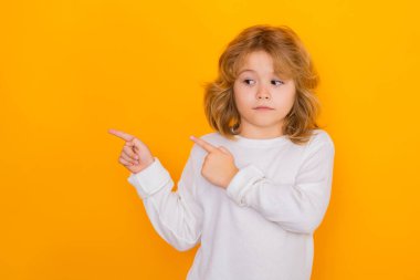 Şaşırmış çocuk sarı izole edilmiş stüdyo geçmişini işaret ediyor. Şok olmuş bir çocuk, reklam teklifleri sunuyor.