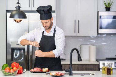 Yakışıklı adam mutfakta yemek hazırlıyor. Yakışıklı, orta yaşlı bir adam mutfakta et pişiriyor. Adam mutfakta yemek hazırlıyor. Mutfak konseptinde sağlıklı yemek ve yemek.