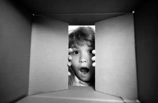 Kid opening package. Child boy age 6 year opening a carton box and looking inside, unpacking concept, surprise unboxing