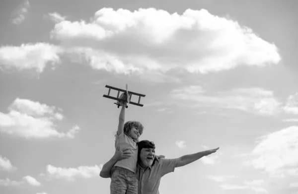Old grandfather and young child grandson having fun with plane outdoor on sky background with copy space. Child dreams of flying, happy childhood with grand dad