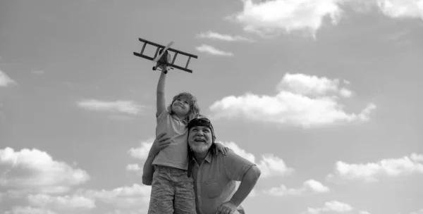 Grandfather and son with toy plane over blue sky and clouds background. Men generation grandfather and grandson playing outdoors