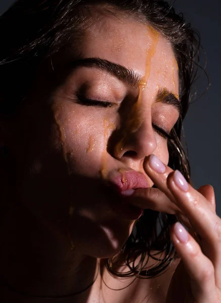 Sensual young woman face with honey drop close up. Sexy model with honey drip on face. Portrait of young woman