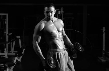 Dambıllar spor salonunda çalışıyor. Dambıllı adam eğitimi. Sağlıklı bir yaşam tarzı. Vücut geliştirme konsepti. Sporcu kasları