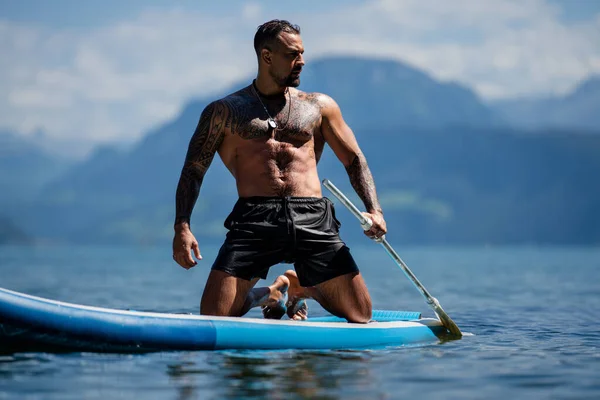 阿尔卑斯山湖上的船桨上的人 湖上有桨的休闲活动 男子划桨冲浪板 肌肉强壮的西班牙男子划桨冲浪者 拉丁男子在船桨冲浪 — 图库照片