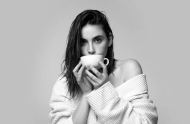 Bornozlu genç kız elinde bir fincan kahve tutuyor. Kahve fincanı ile gülümseyen mutlu kadın, stüdyo izole