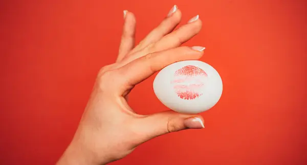 Print of red lips on white egg. Red lip imprint on easter egg on red background. Lipstick kiss print