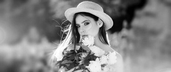 Outdoor fashion photo of beautiful young woman surrounded by flowers. Summer model holding flowers in hands outdoors