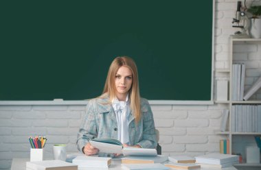 Lise öğrencisi sınıfta İngilizce ya da matematik öğreniyor. Kopya alanı ile karatahta arkaplan üzerine kitap okuyan ciddi öğrenci