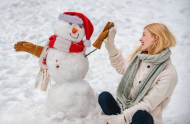 Karlı kış yürüyüşünde bir kardan adamla oynayan mutlu kız. Kadınlar için kış kıyafetleri. Mutlu kız kış portresi
