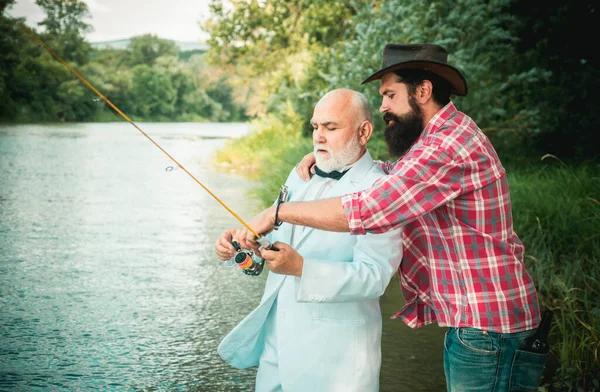Father and mature son fisherman fishing with a fishing rod on river. Portrait of senior businessman fishing in white suit and bowtie with fishing rod, spinning reel on river