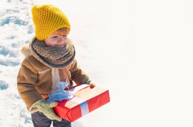 Kışlık elbiseli çocuğun elinde Noel hediyesi var. Karlı bir kış parkında gezinen bir çocuk. Güzel kış doğası. Harika bir kış parkı. Şirin yüzlü sevimli bir çocuk. Boş kopyalama alanı olan ptoto