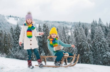 Komik çocuk ve kız kışın kızakla eğleniyorlar. Karda oynayan sevimli çocuklar. Çocuklar için kış aktiviteleri. Kış çocukları eğlence