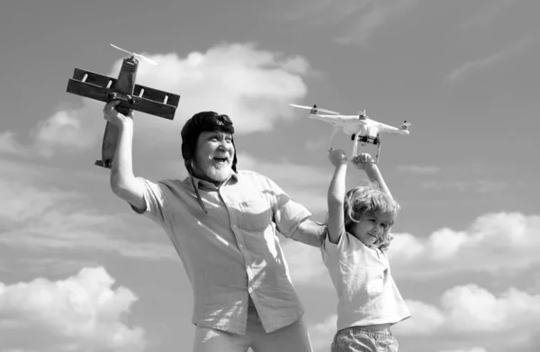 Grandson child and grandfather hold plane and drone quad copter against sky. Child pilot aviator with plane dreams of flying. Family Relationship Grandfather and child