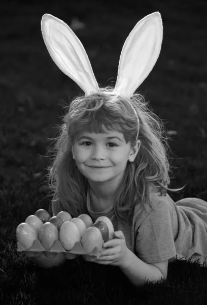 Kids boy in rabbit costume with bunny ears hunting easter eggs. Child gathering Easter eggs, laying on grass