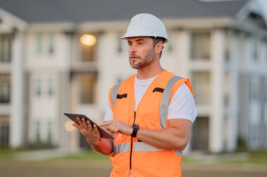 Tabletli mühendis, bina teftişi. Miğferli inşaat işçisi yeni bir ev inşa etti. Mühendis, inşaat üniforması ve başlık giyiyor. Foreman açık hava portresi. 40 'ların işçisi