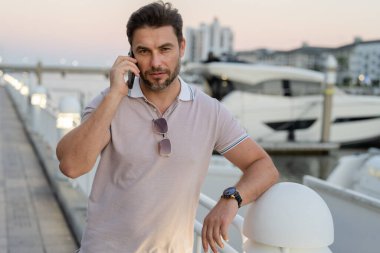 Büyük şehirde telefonda konuşan yakışıklı bir adamın portresi. Sokakta telefonla konuşan, günlük kıyafetli seksi bir adam. Şehir yaşam tarzında başarılı bir erkek model. İş telefonu görüşmesi