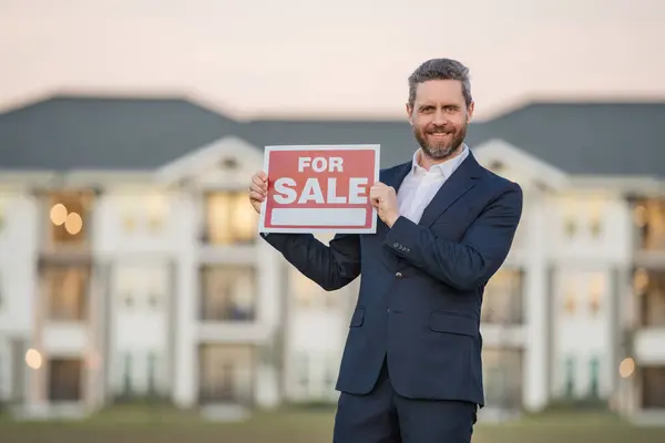 House for sale. Real estate purchase and sale concept. Real estate services. Confident man in suit, real estate agent, professional realtor offering new dwelling real estate house to buyer