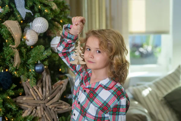 Happy kid decorating Christmas tree. Happy funny child in winter pajama near Christmas tree at morning. Christmas and New Year concept