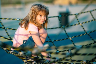 Child climbing the net. Little boy climbs up the ladder on the playground. Child climbs up the ladder. Little caucasian boy hanging on the monkey bar by his hand to exercise at outdoor playground