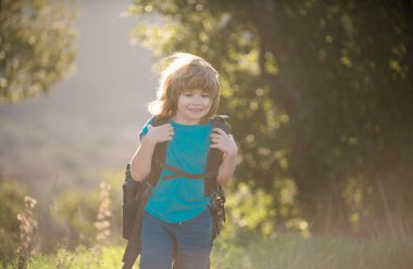 Tepelerde sırt çantasıyla yürüyüş yapan bir çocuk yürüyüşçüsü. Dağlarda yürüyüş malzemesi olan sevimli bir çocuk.