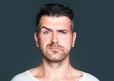 Tüylü ve kaşlı yakışıklı bir adamın portresi. Gri arka planda, dikey resimde, stüdyoda ileri bakan bir model.